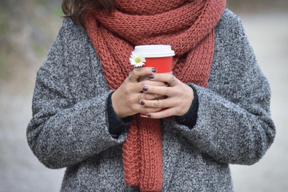 Una chica abrigada sujetando un café, en una imagen de archivo.