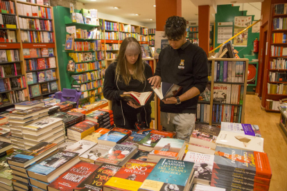 Dos joves, aquesta setmana a la llibreria Caselles de Lleida davant d’un expositor de novetats literàries.