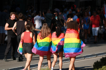 Cuatro chicas de espaldas con la bandera LGTBI durante el desfile del Pride de Barcelona