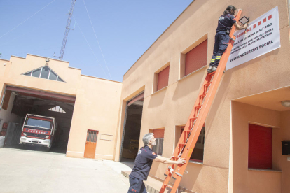 Dos bombers voluntaris penjant ahir la pancarta al parc d’Agramunt.