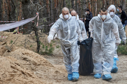 Treballadors ucraïnesos transporten cossos de tombes trobades el setembre a Izium, a Khàrkiv.