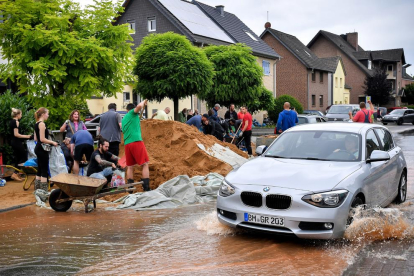 Un coche pasa delante de varios alemanes que limpian los destrozos de las indundaciones, ayer. 