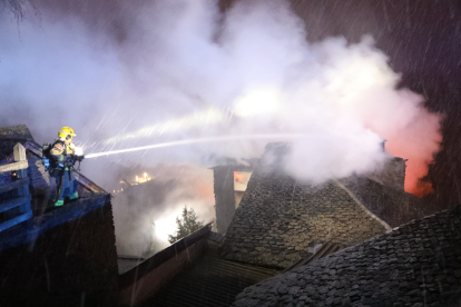 Un bomber llançant aigua ahir a la tarda sobre la teulada de l’habitatge, al poble de Surp.