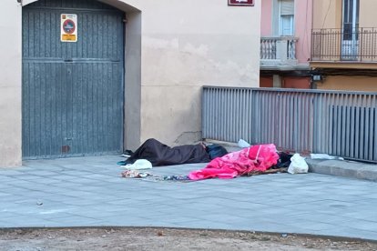 Dos persones dormint al ras a la plaça del Dipòsit.