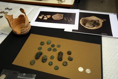 Dos monedes restaurades al costat d'altres peces pendents de tractar, vora la gerra de ceràmica on estaven amagades, al Laboratori d'Arqueologia de la UdL.
