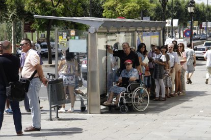Usuaris de l’autobús ‘refugiats’ a la zona d’ombra d’una marquesina ahir al migdia.