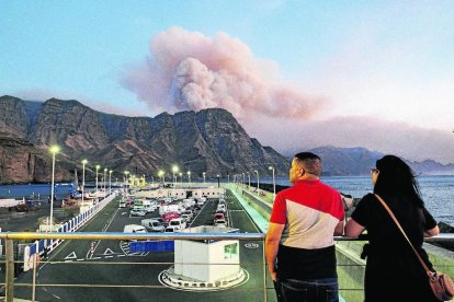 Dos personas observan al caer la tarde la columna de humo reactivada en el Pinar de Tamadaba