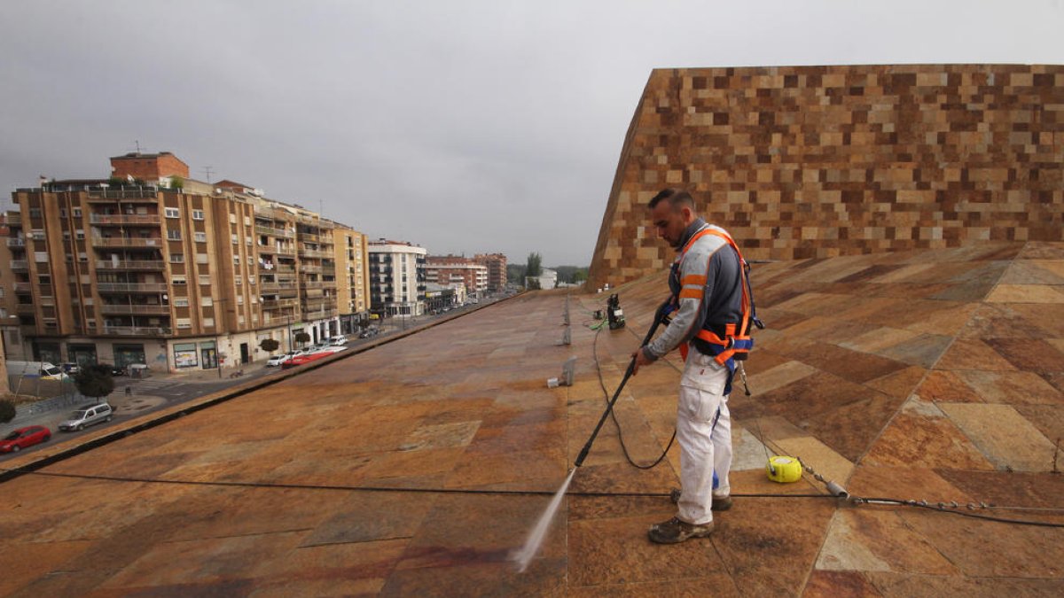 Un operari a la coberta de l’edifici netejant la pedra amb aigua a pressió.