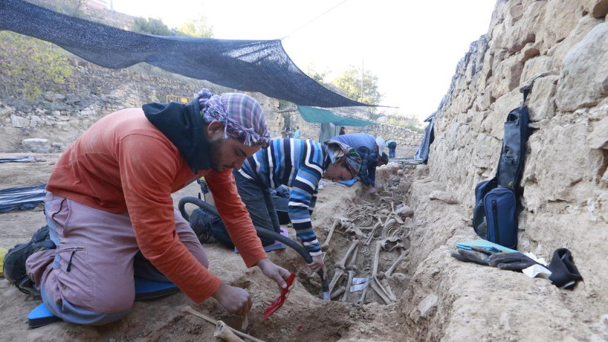 L’equip d’arqueòlegs i antropòlegs treballant a l’excavació, amb diverses rases, i vista de les restes d’un soldat franquista.
