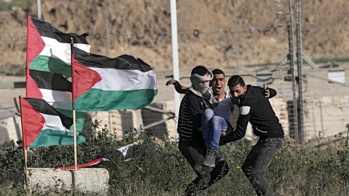 Varios manifestantes palestinos retiran a un joven que resultó herido en la frontera entre Israel y Gaza.