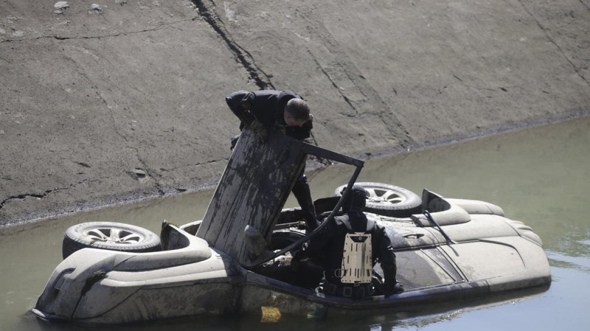 Imagen de los dos vehículos en el interior del canal. En la foto de la derecha, los buzos de los Mossos inspeccionando uno todoterreno. 
