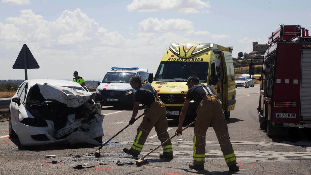 Dos bombers, treballant al lloc de l’accident al costat del cotxe en el qual viatjava la víctima mortal.