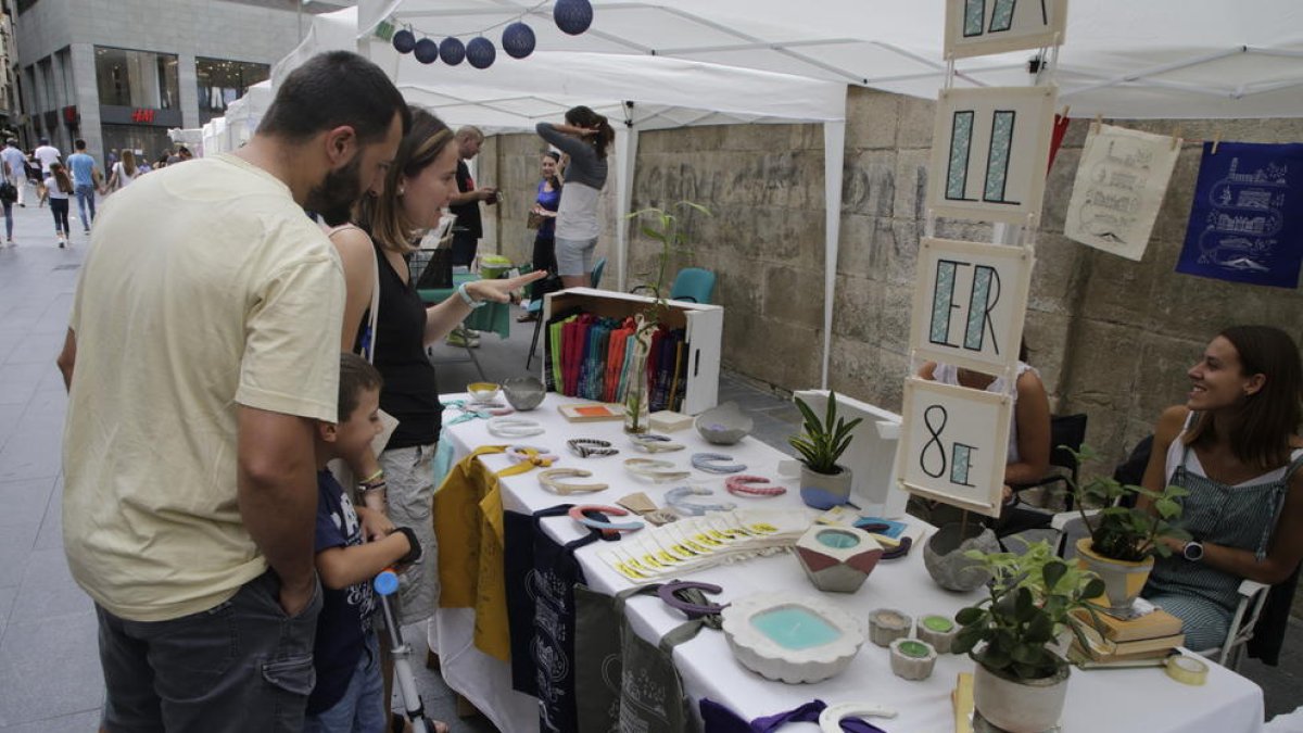 Una família observa els productes d’un dels 13 artistes que van mostrar les seues obres davant de l’IEI.