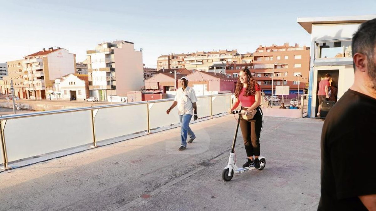 Una usuària circula amb un patinet elèctric a la passarel·la de l'estació, on està permès fer-ho.