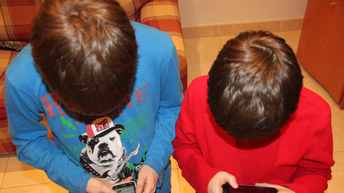 Imagen de dos niños jugando con el teléfono móvil en casa. 