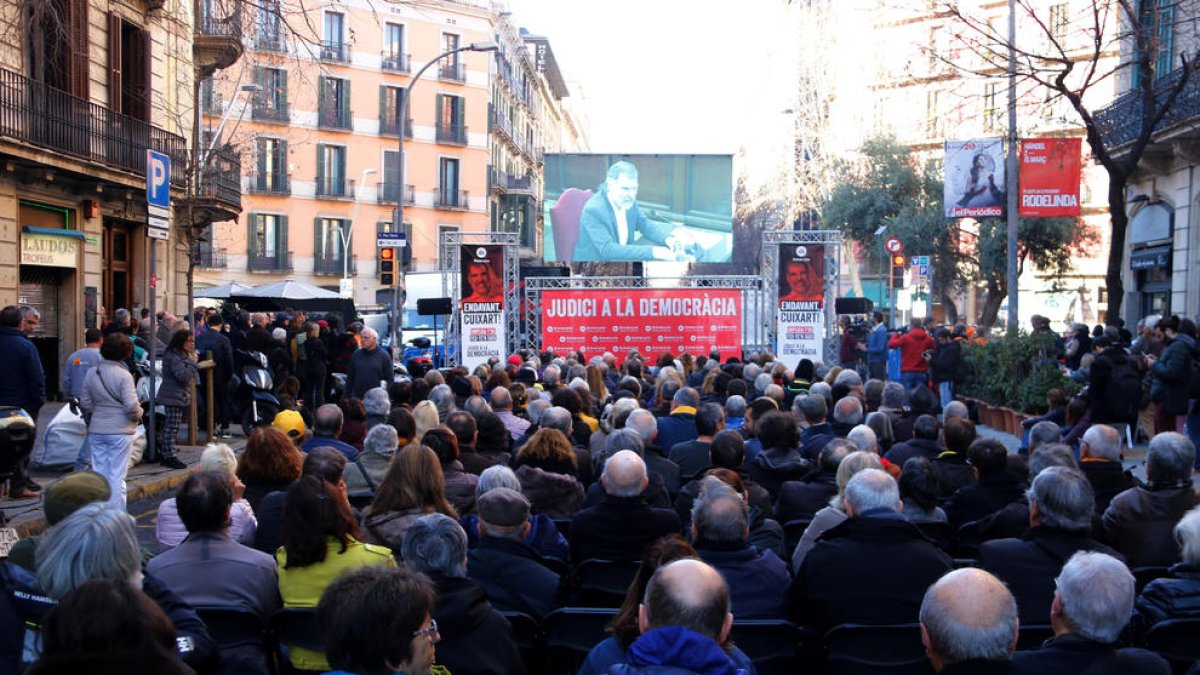 Centenars de persones segueixen la declaració de Jordi Cuixart al Suprem amb una pantalla gegant des de davant de la seu d'Òmnium a Barcelona. Imatge del 26 de febrer del 2019.