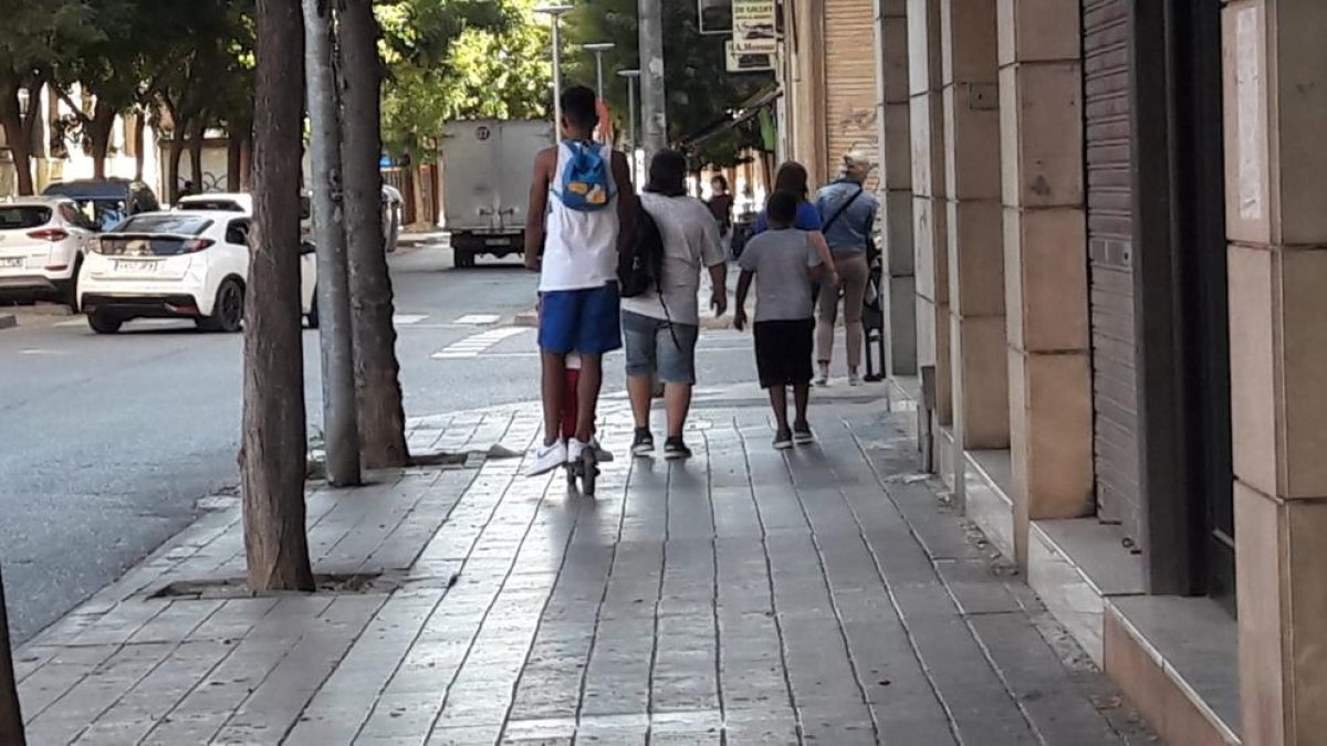 Un joven y un niño en patinete eléctrico sin casco y por la acera. 