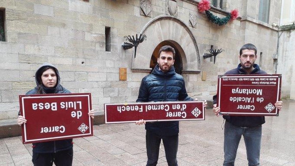 Tres joves sostenen de cap per avall les plaques dels carrers arrencades.