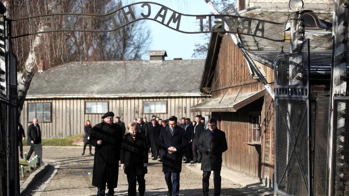 Merkel cruza la entrada del campo de concentración de Auschwitz, bajo el siniestro cartel “El trabajo os hará libres”.