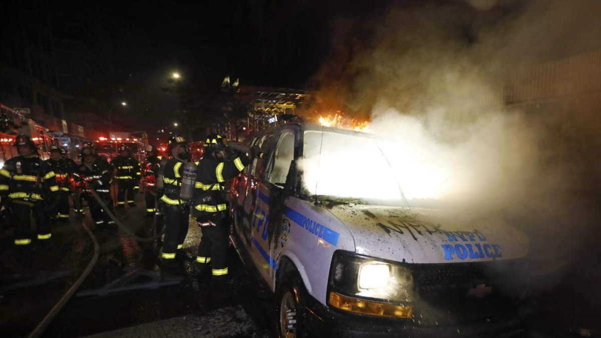 Els bombers de Nova York apaguen les flames d’un cotxe patrulla durant les protestes.
