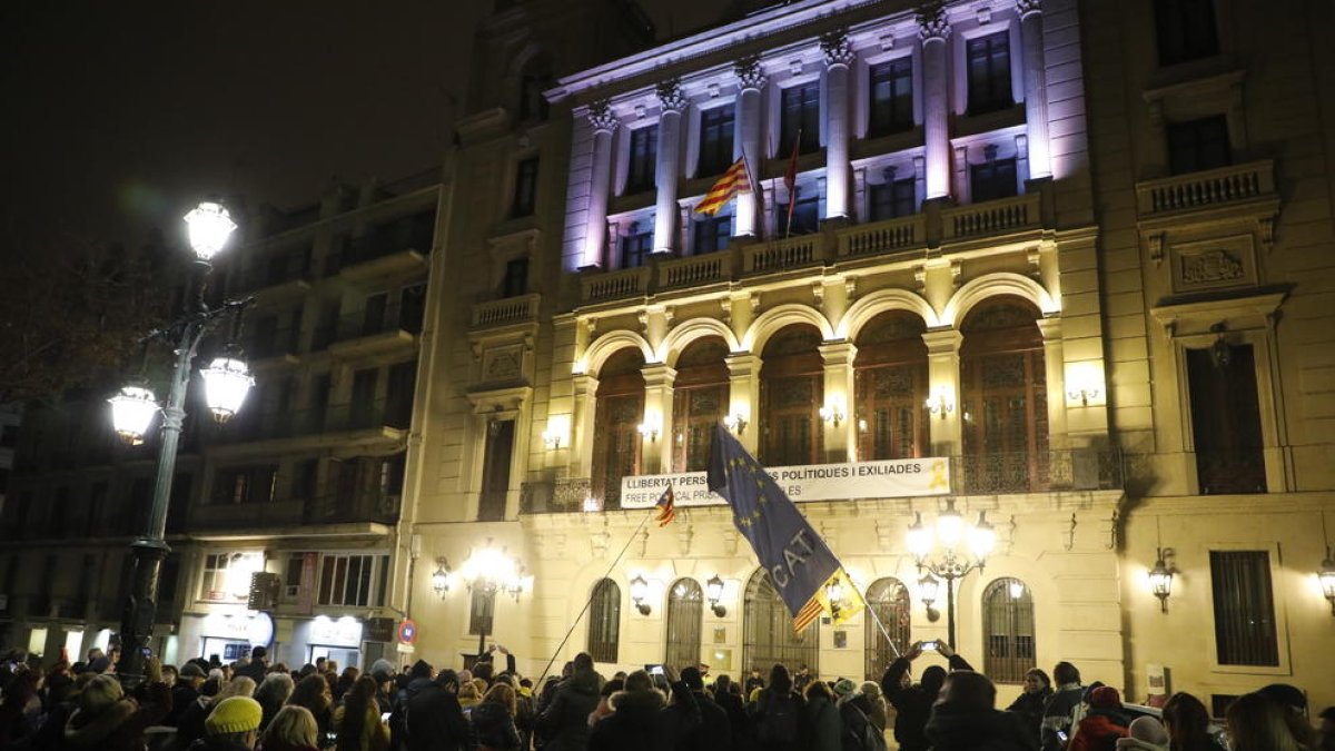 Los concentrados observan cómo tres encapuchados arrían la bandera española de uno de los mástiles del balcón de la Paeria.