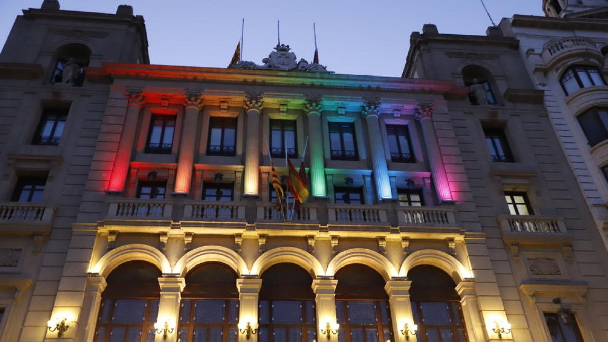 Bandera multicolor al balcó de l’ajuntament de les Borges i façana de la Paeria de Lleida il·luminada amb els colors de l’arc de Sant Martí.