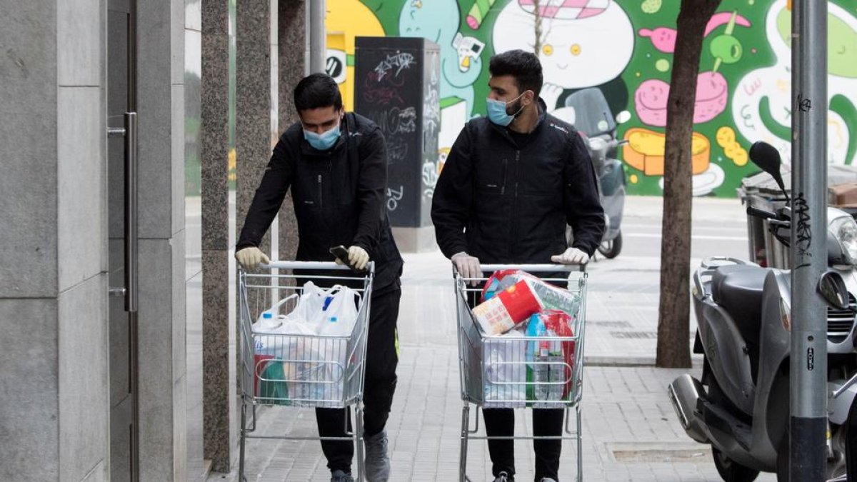 Dos trabajadores de un supermercado de Barcelona llevan la compra a casa de unos clientes.