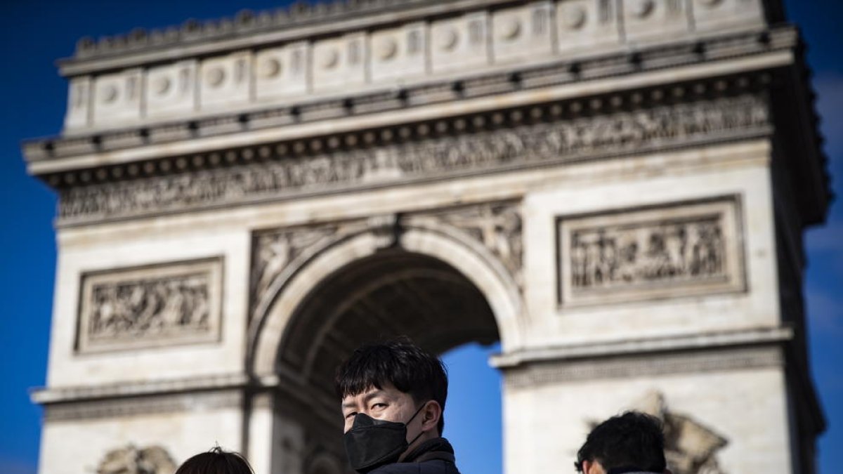 Diversos turistes passegen davant l’Arc del Triomf de París.