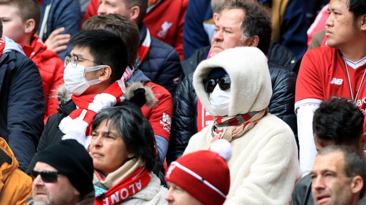 Aficionados viendo ayer el Liverpool-Bournemouth con mascarillas por temor al coronavirus.