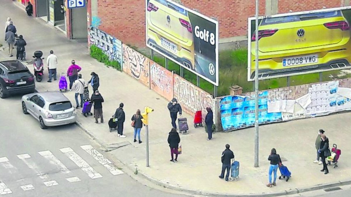 Ciutadans fan cua mantenint la distància de seguretat davant d’un supermercat al centre urbà.