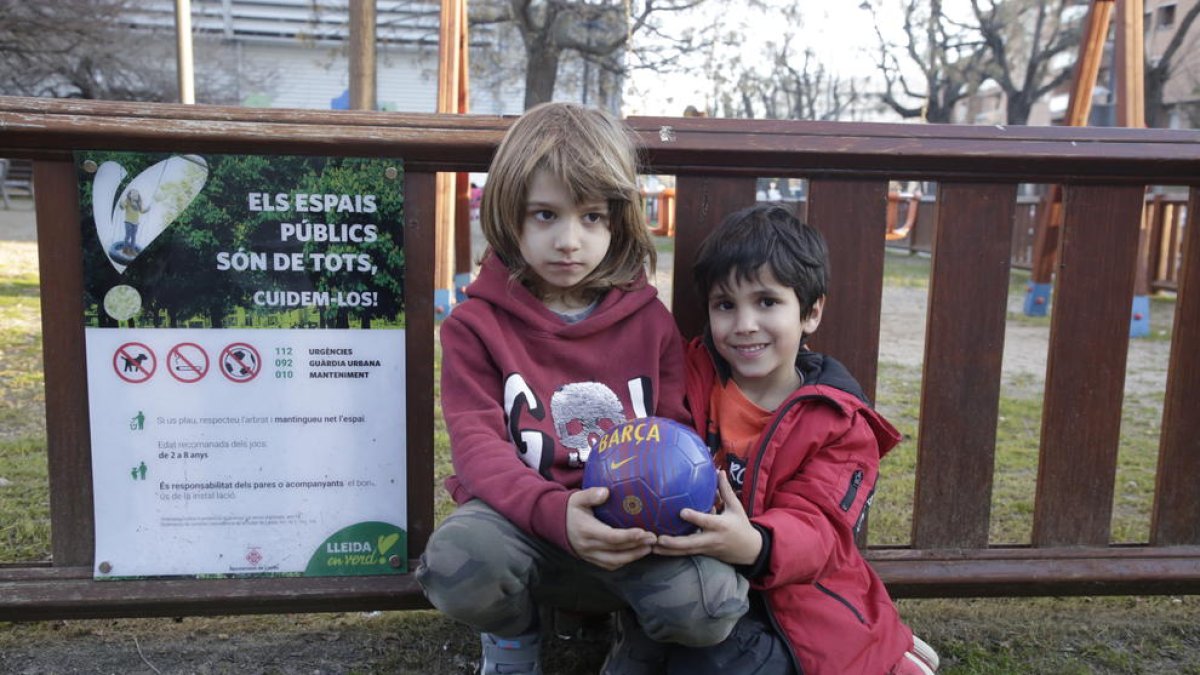 Dos niños pequeños con una pelota ayer en una plaza de Balàfia ante un cartel con la prohibición.