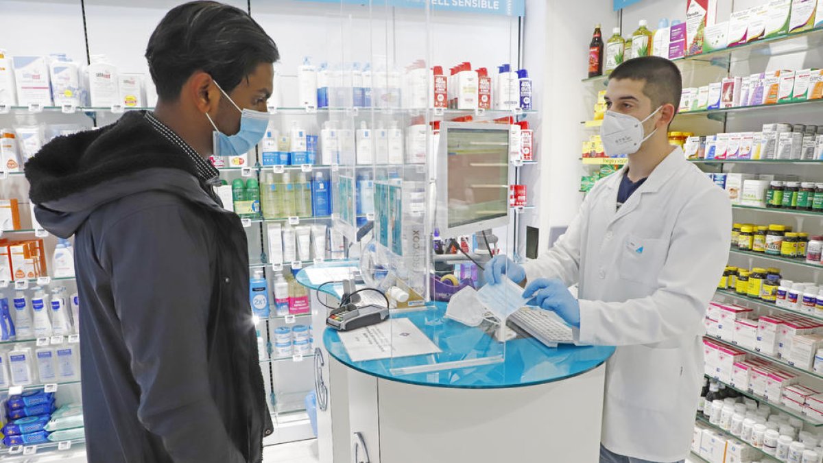 Imagen de un empleado de una farmacia de Lleida mostrando las mascarillas que venden a un cliente.