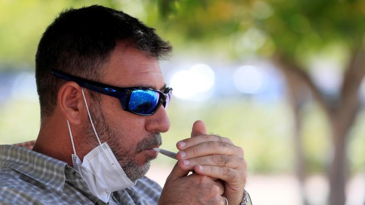 Un fumador s’encén un cigarro en un parc madrileny.