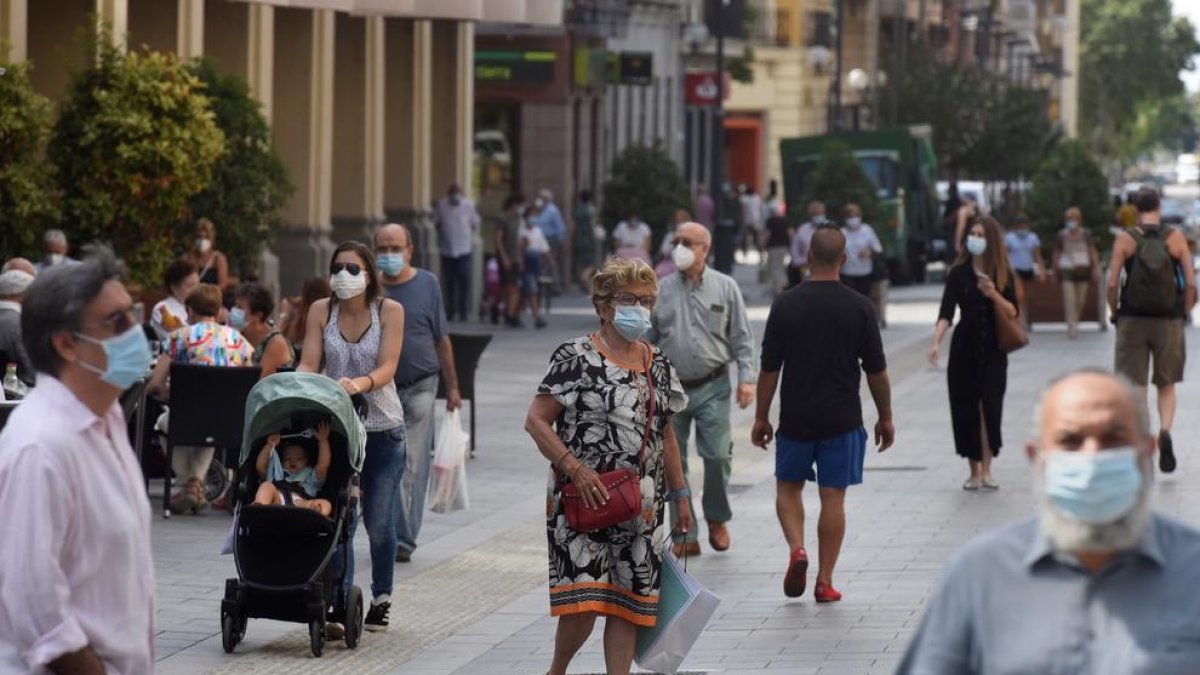 Varias personas pasean con la mascarilla puesta por una concurrida calle de Huesca. 