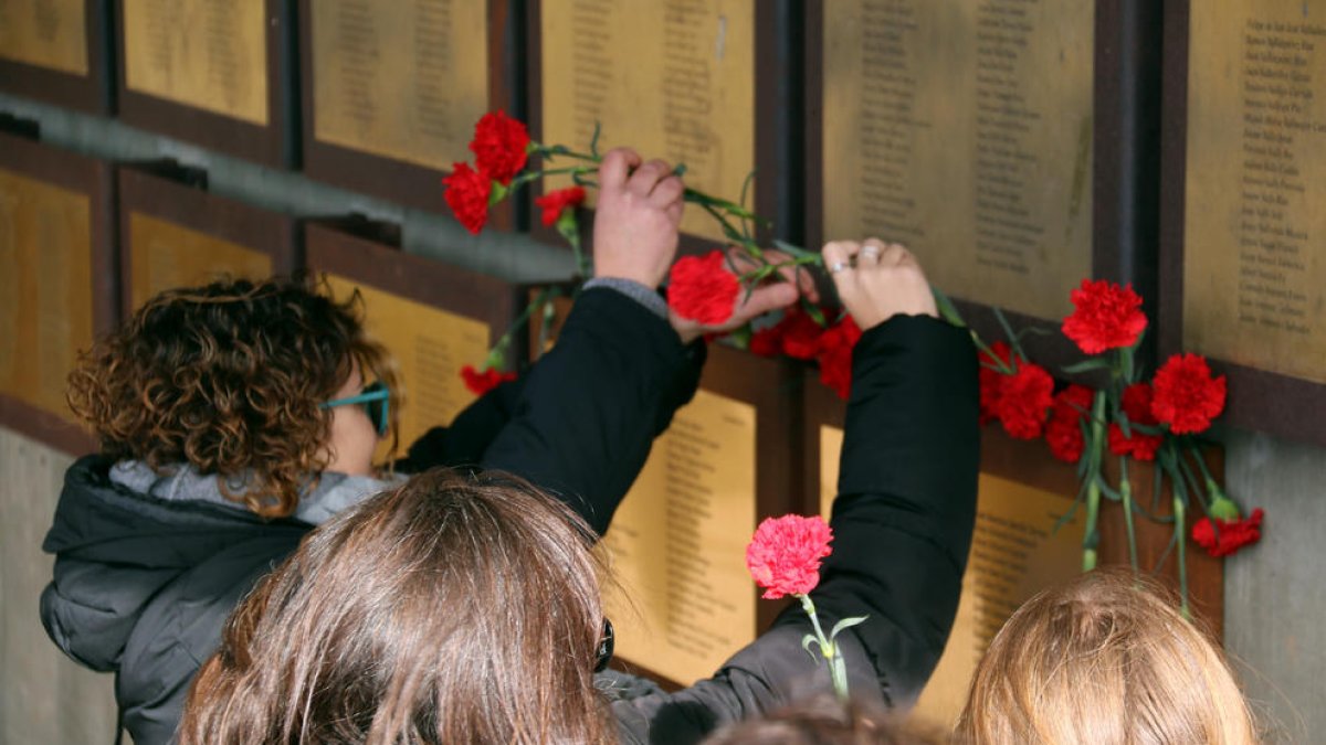 Familiares depositando claveles rojos bajo las placas que recuerdan a las víctimas de la Guerra Civil.