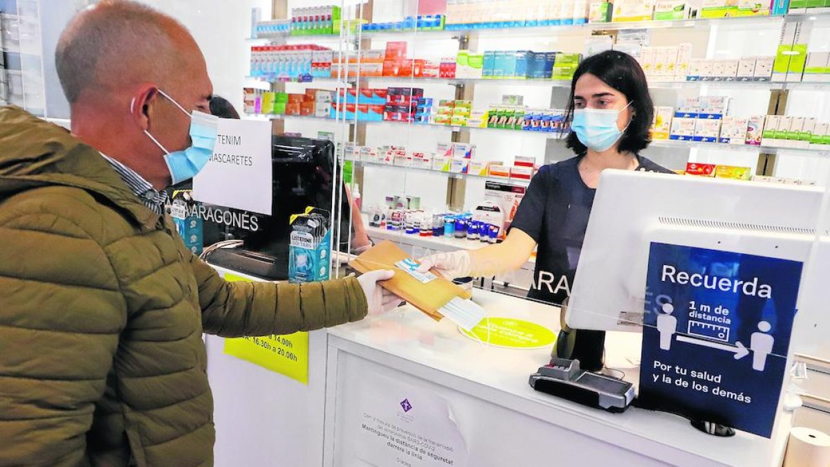 Un cliente recogiendo una mascarilla gratis con su tarjeta sanitaria en Lleida.