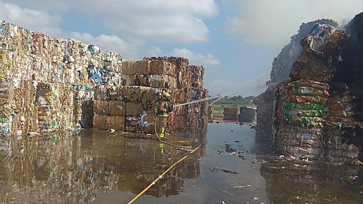 Un bomber tira aigua sobre les bales afectades pel foc.