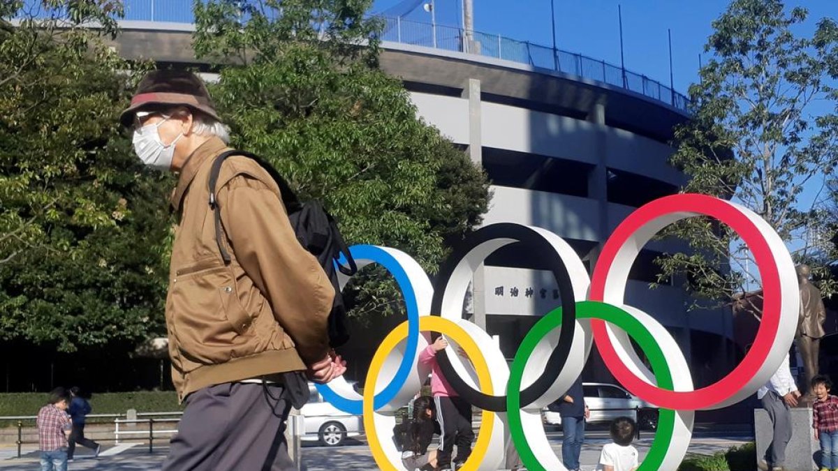 Un hombre protegido por una máscara pasa junto a los anillos olímpicos instalados en Tokio.