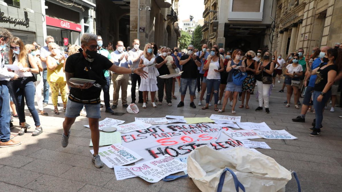 A l’esquerra, tres persones esmorzen en un banc de l’Eix després de demanar menjar per emportar-se. A la dreta, un manifestant trenca plats davant l’edifici de l’ajuntament.