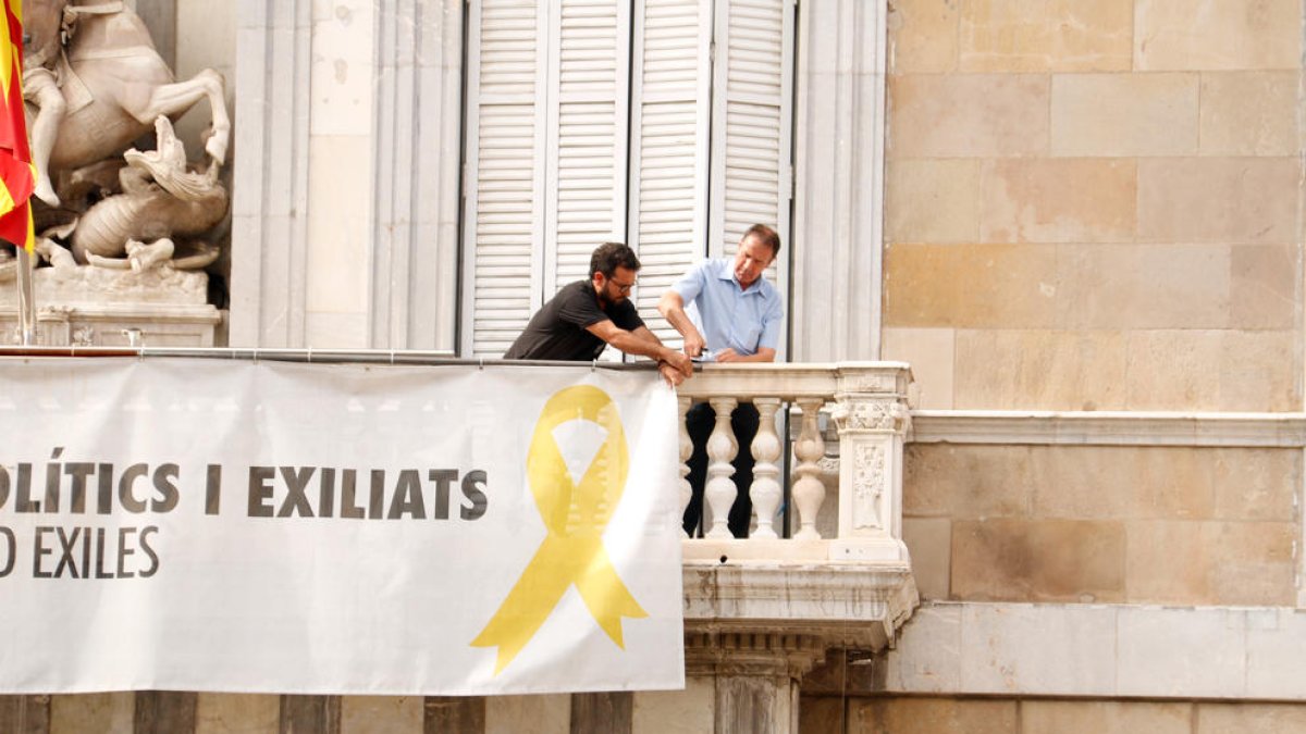 Dos treballadors de la Generalitat retiren la pancarta de Palau a favor dels presos després de l'ordre del TSJC als Mossos