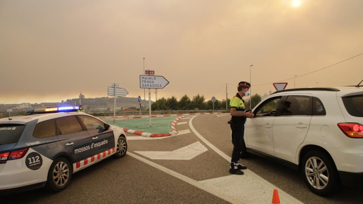 Mossos d’Esquadra se protegían ayer de las cenizas con máscaras para informar a los conductores del corte de la carretera C-12 en Maials.