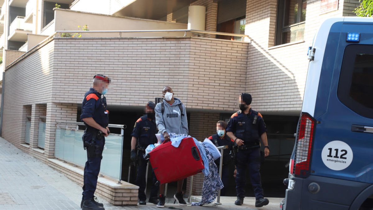 Un dels adults desnonats treu els seus estris al carrer davant la mirada de diversos mossos,