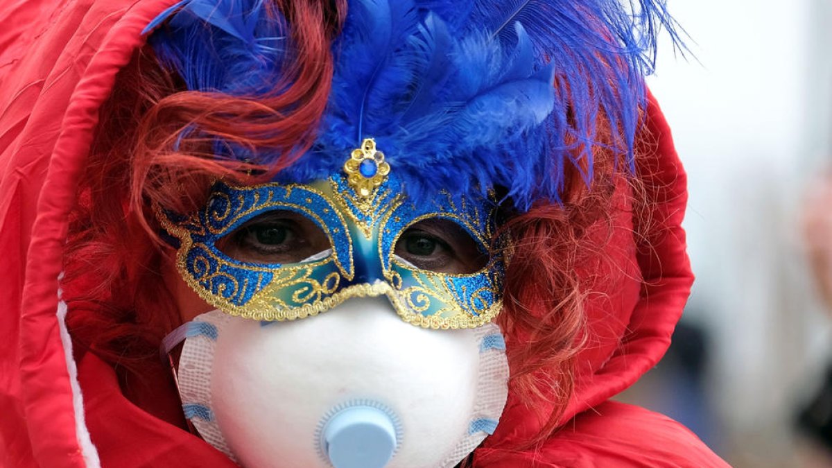 Una persona amb la màscara de Carnaval i una mascareta de paper pel coronavirus.