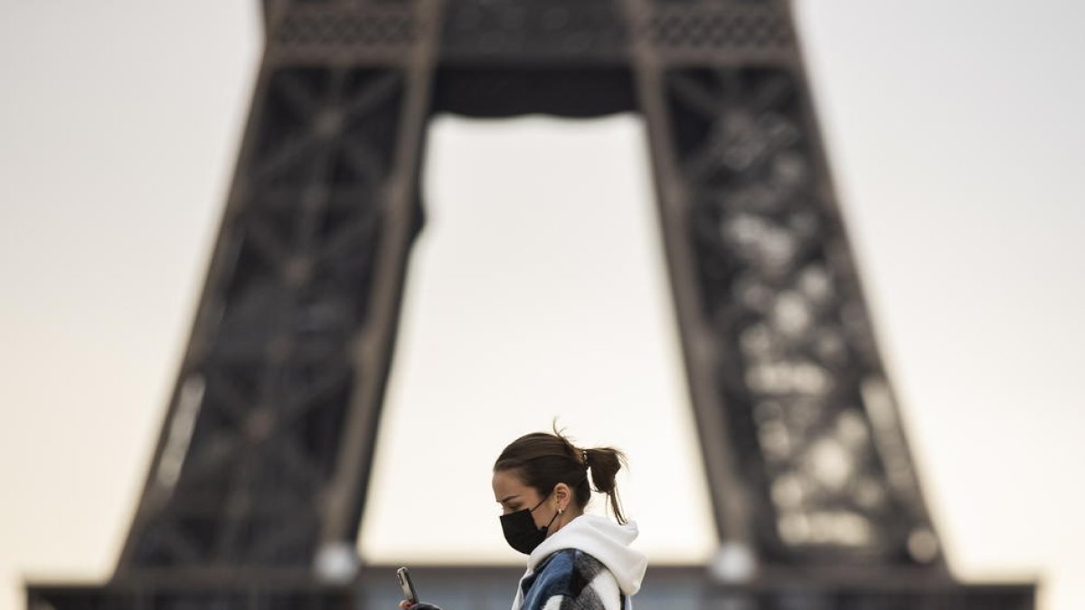Una dona passeja amb mascareta davant de la Torre Eiffel.