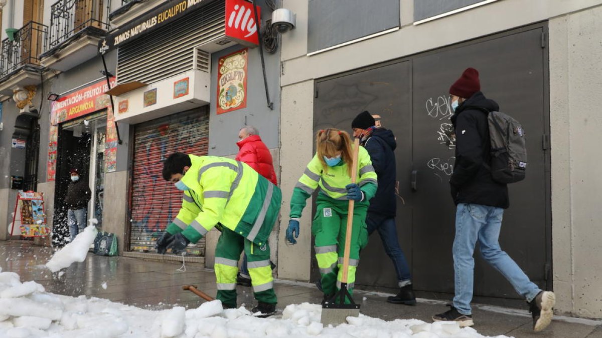 Dos operarios trabajan en la retirada de la nieve y el hielo de la calle.