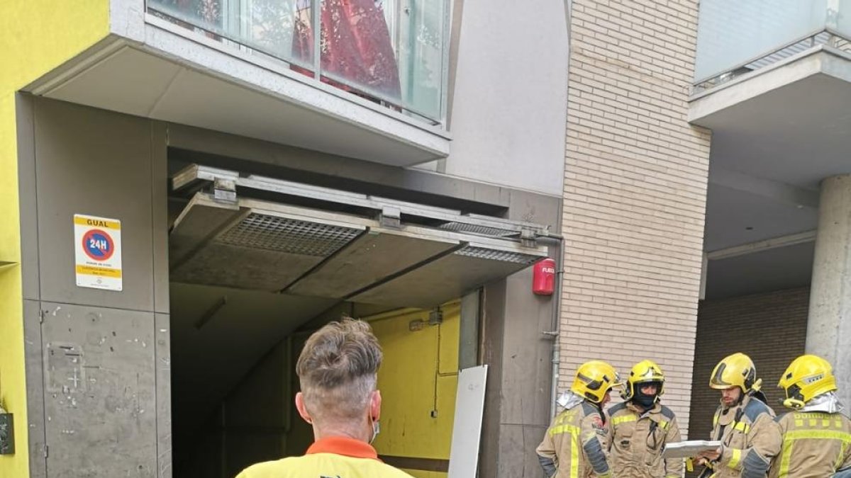 Un profesional del SEM y bomberos ante el parking donde se incendió el coche.