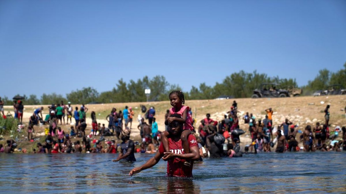 Un migrante haitiano carga a una niña mientras cruza a pie el Río Grande, que separa México y EEUU.