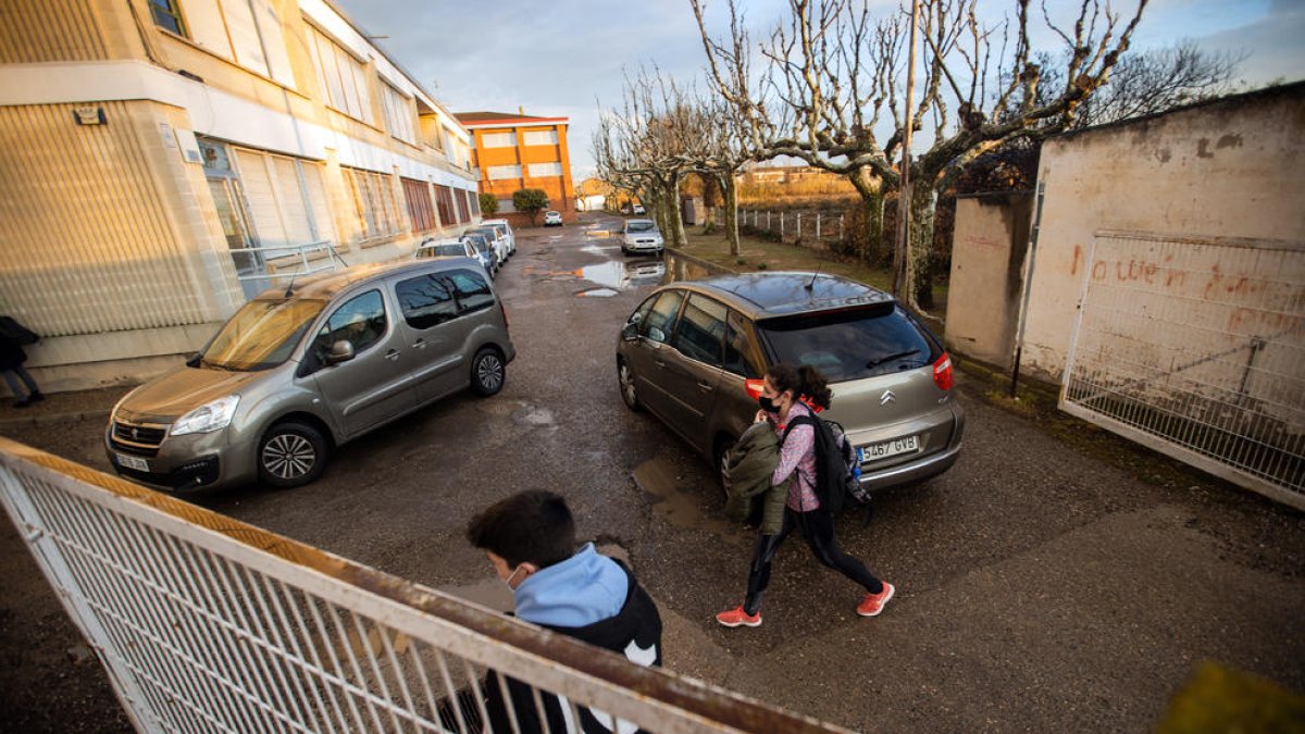 Coches y alumnos en el aparcamiento que da acceso a la escuela.