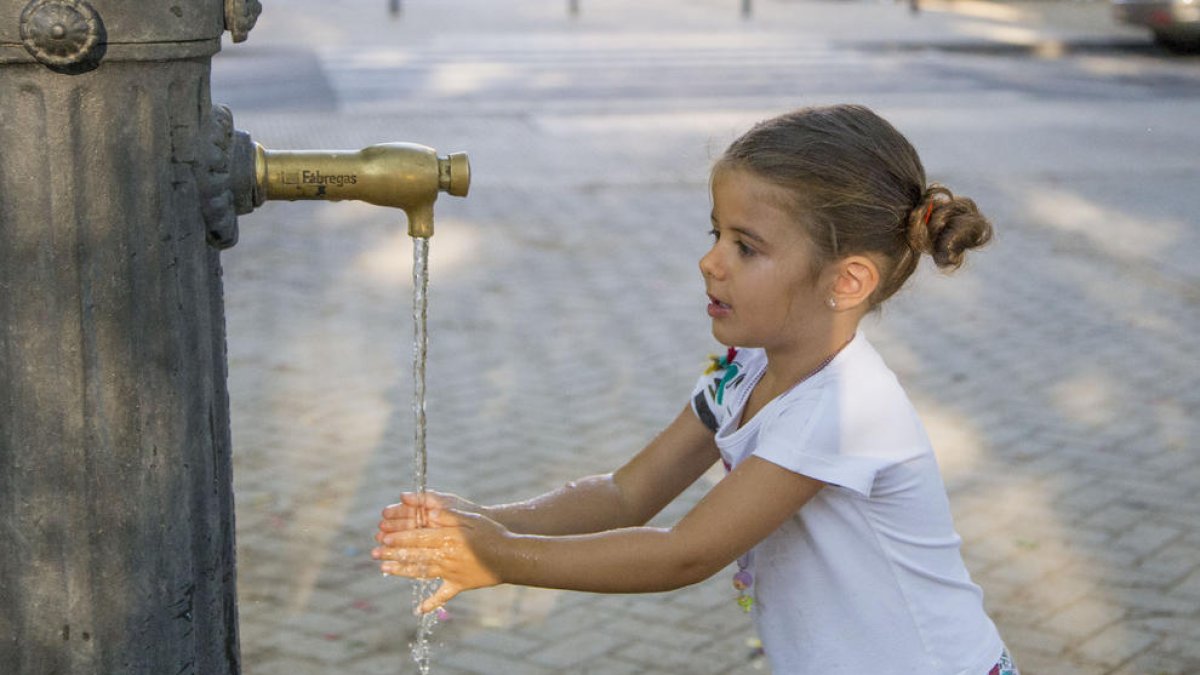 Una nena refrescant-se en una font el mes d’agost passat.