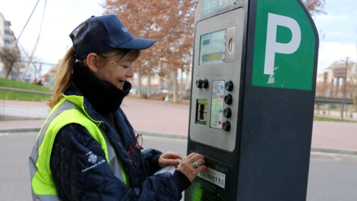 Una controladora de la zona blava de Lleida canvia l'adhesiu amb el nom de l'antiga concessionària pel de l'EMAU en un parquímetre.